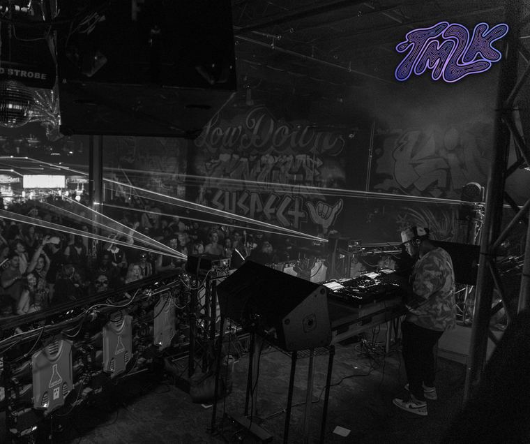 Black-and-white view from behind the booth across the crowd and lasers